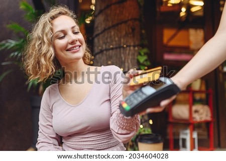 Young woman wearing casual clothes at cafe buy breakfast sit at table hold wireless modern bank payment terminal to process acquire credit card payments relax in restaurant during free time indoors. Royalty-Free Stock Photo #2034604028
