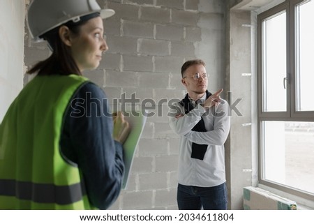 two engineers, a man and a woman in white helmets and green protective vests, work at the construction site, professional and licensed engineers in construction and fire safety technology take