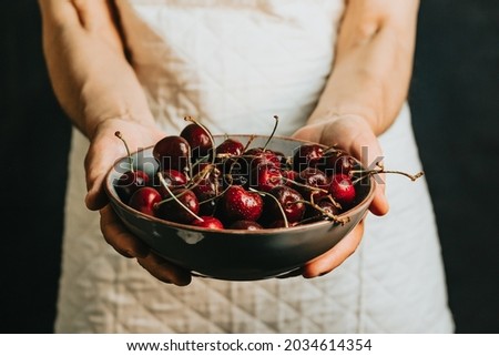 Old waitress offers and holds a bunch of cherry in a bowl, fruits, healthy life, good eating, mediterranean concepts, copy space, vertical image