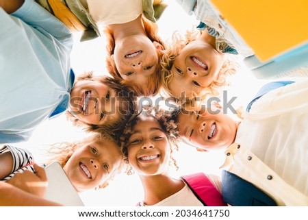 Low angle view of a group of mixed-race multi-ethnic classmates schoolchildren kids standing in round ring together smiling before classes lessons at school. Royalty-Free Stock Photo #2034641750