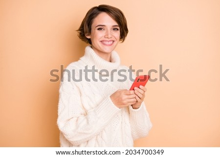 Photo portrait of pretty girl in sweater using mobile phone smiling isolated on pastel beige color background