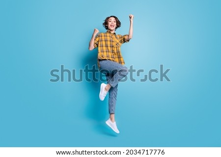 Photo of cheerful lady jump gain achievement wear plaid shirt jeans shoes isolated blue color background