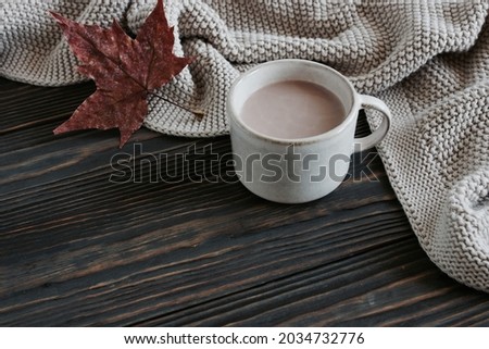 Autumn background. Beige knitting  scarf, autumn dry leaf and cocoa cup top view with copy space on brown wooden background . Autumn cozy template backdrop rustic style.