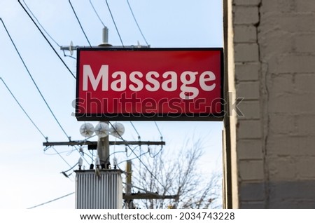A red massage sign juts out from the side of a brick building and below overhead electrical wires in the suburb of Glenhuntly, Melbourne, Australia.