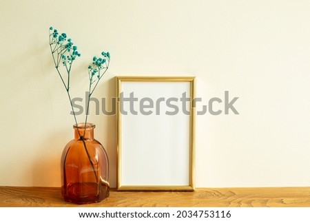 Gold photo frame and dry flowers on wooden table. beige wall background. home interior