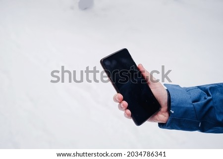 cell phone in a man's hand against a beautiful in the winter snow-covered forest.. winter season