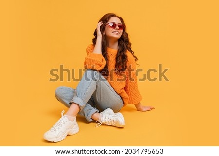Pretty hipster red head girl in stylish autumn autfit posing over yellow background. 