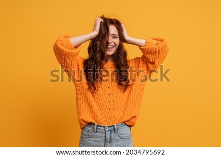 Excited young girl in  orange  sweater  fooling around in studio jumping with fluttering hair isolated on yellow rbackground. People sincere emotions lifestyle.