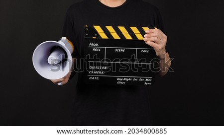 Black and yellow Clapper board or movie slate and Megaphone in man hand isolated on black background.
