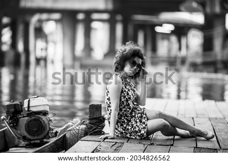 Young Asian woman sits on a wooden river pier. Black and white photo.