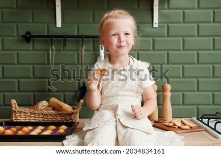 Little happy blonde girl eating heart shaped cookies in the kitchen at home. soft focus