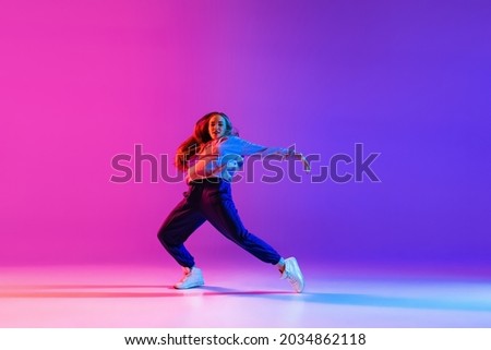 Street dynamics. Young beautiful hip-hop girl dancing isolated on neon studio background. Sport achievement, spirit of expression. Concept of dance, youth, hobby, dynamics, movement, action, ad