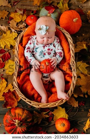 Baby in a wicker basket holding a pumpkin in her hands 