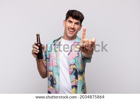 young man with a beer smiling proudly and confidently making number one pose triumphantly, feeling like a leader