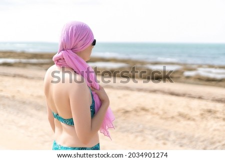 Woman with pink scarf for cancer looking at the sea in bikini from the beach