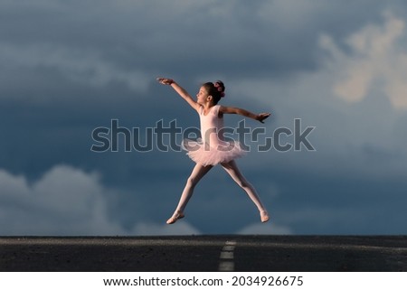 Little ballet dancer girl wearing a pink tutu jumping in the horizon of the road. Dramatic sky with copy space in the background