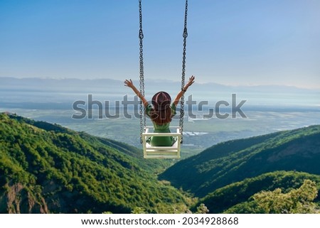 Carefree free woman traveler with open arms rides on a swing against background of beautiful landscape and enjoying freedom and happy moment life Royalty-Free Stock Photo #2034928868