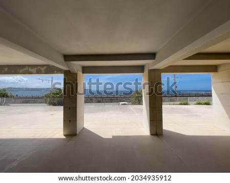 View to sea in sunny day under building in wall-less ground floor frames between concrete pillars 