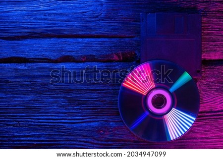 Cd disk and floppy disk in the neon lights on the wooden table flat lay background with copy space.