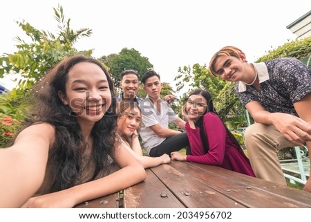 Six southeast asian friends taking a selfie on a bench outdoors.Cheerful and upbeat mood. Gen Z people having fun together.