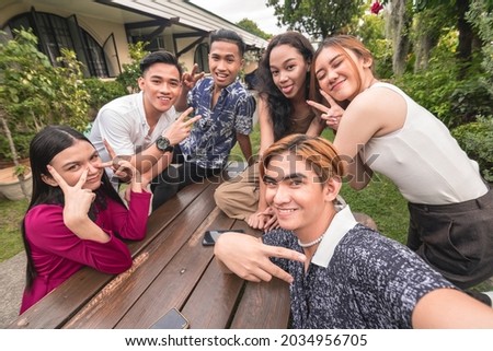 Six southeast asian friends taking a selfie on a bench outdoors.Cheerful and upbeat mood. Gen Z people having fun together.
