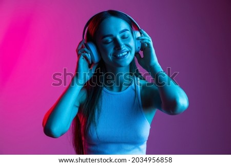 Close-up portrait of young beautiful girl wearing headphones and listening music on gradient pink purple background. Creative lifestyle, art importance. Concept of youth culture, music, art, ad