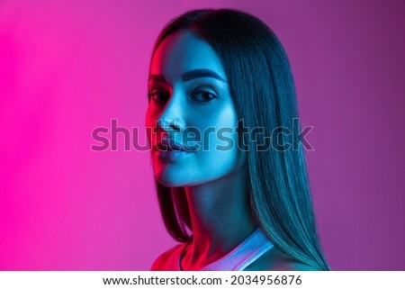 Side-viewed close-up portrait of young beautiful girl attentively looking forward on camera on pink purple background. Youth culture. Concept of facial expressions, photography, youth, beauty, ad