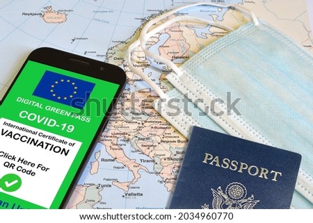 The digital green pass of the european union with the QR code on the screen of a smartphone  over maps with a surgical mask and a passport. Immunity from Covid-19. Travel without restrictions.