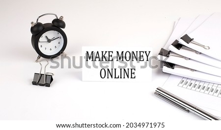 Card with text MAKE MONEY ONLINE on a white background, near office supplies and alarm clock. Business