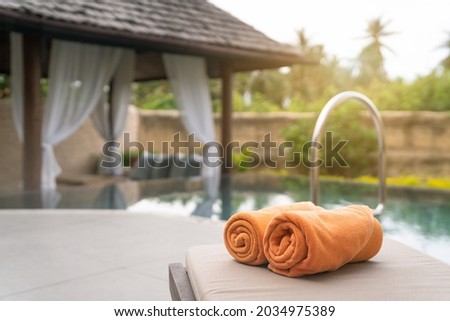 Folded orange towels on lounge chair by the  pool side, private pool villa, vacation Royalty-Free Stock Photo #2034975389