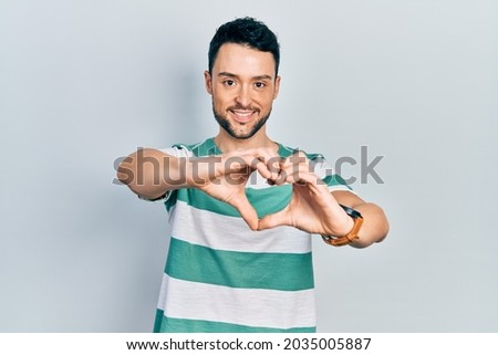 Young hispanic man wearing casual clothes smiling in love doing heart symbol shape with hands. romantic concept. 