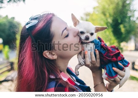 The girl holds a mini chihuahua in her arms. Kissing your pet. The dog and the owner are dressed in the same color. Clothes for animals. Love and care for four-legged pets.