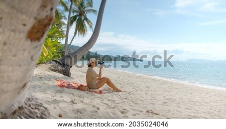 Young brunette woman have a picnic on the beach under the palms, she sits on the sand, empty beach