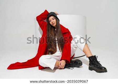 Fashionable  model in stylish  hat, red coat and boots  posing on white background in studio.   Royalty-Free Stock Photo #2035039067