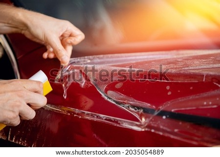 Concept Transparent protection for paint. Process of pasting hood of red car with protective vinyl film from gravel chips and scratches. Royalty-Free Stock Photo #2035054889