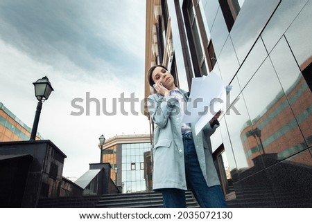 Modern business woman talking on the phone while holding documents on the stairs