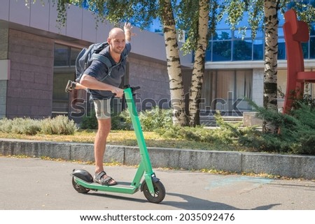 A man rides a rented electric scooter, standing on one leg. The guy is riding a scooter and having fun.
