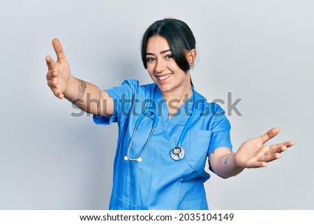 Beautiful hispanic woman wearing doctor uniform and stethoscope looking at the camera smiling with open arms for hug. cheerful expression embracing happiness. 