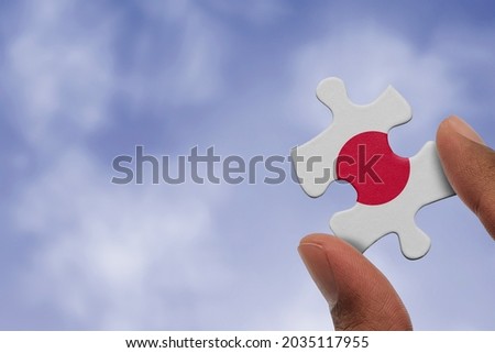 Hand holding piece of jigsaw puzzle with flag of Japan. Jigsaw puzzle of Japan flag on sky background.