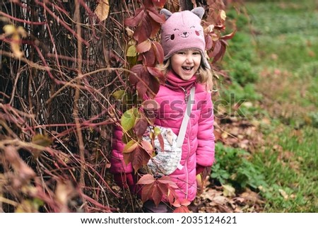 Little girl having fun in beautiful park with dry yellow and red leaves. Autumn family walk in forest.