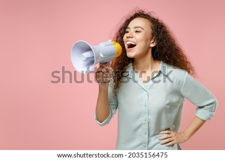 Young black african american surprised excited cute rich curly woman 20s wearing blue shirt screaming in megaphone shouting hot news look aside isolated on pastel pink color background studio portrait
