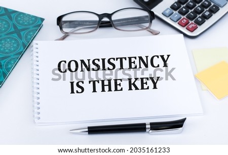CONSISTENCY IS KEY text on a notebook next to glasses, calculator, black pen and papers