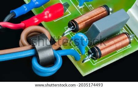 Circuit board detail with inductors or capacitors on black background. Electronic components as ferrite bead with insulated wires, coils or faston terminals. RF filter of electric motor supply module. Royalty-Free Stock Photo #2035174493