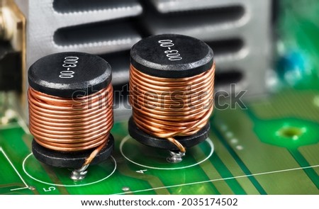 Closeup of electronic coils and metal cooler on green printed circuit board detail. Ferromagnetic inductors with copper wire winding or aluminum heat sink on PCB. Components in electrical engineering. Royalty-Free Stock Photo #2035174502