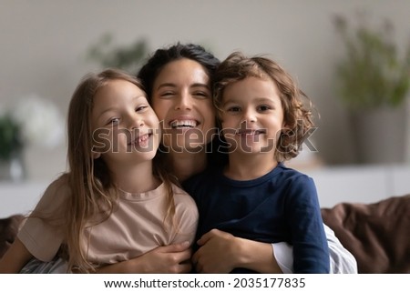 Portrait of happy mother hugging two cute little kids. Joyful affectionate mom cuddling sweet sibling son and daughter, looking at camera with toothy smile. Family relationship, motherhood. Head shot Royalty-Free Stock Photo #2035177835
