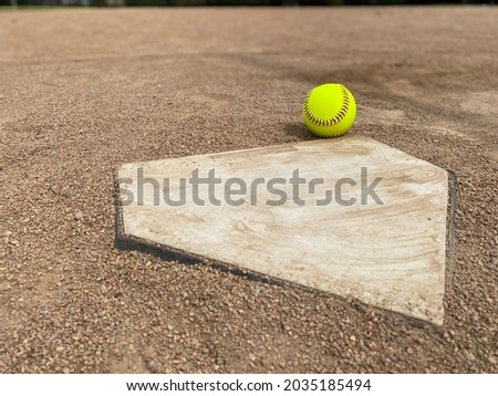 Yellow softball at home plate on a dirt infield with copy space