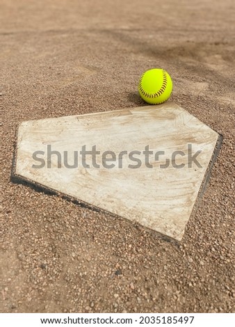 Yellow softball at home plate on a dirt infield with copy space