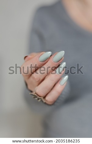 Female hand with long nails light gray manicure and a bottle of nail polish