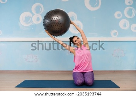 a woman in sportswear is engaged with a fitball on a rug in the studio