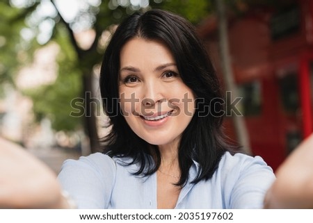 Close up portrait of a beautiful caucasian mature middle-aged woman mother wife taking selfie photo having video call on webcam using smart phone outdoors in park